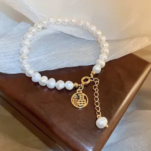 Baroque freshwater pearl bracelet with gold metal charm and extension chain detail.