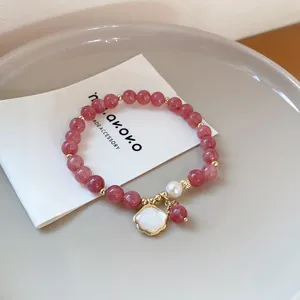 Close-up of strawberry crystal and pearl bracelet with shell pendant detail and golden beads.