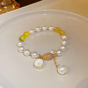 Close-up detail of the elegant fashion pearl bracelet with shell pendant and yellow gemstone accents.