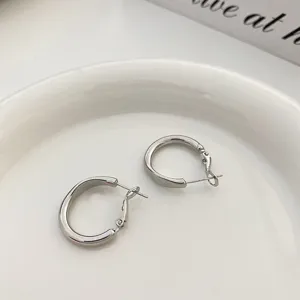 Primo piano dettagliato di eleganti orecchini a cerchio in metallo argentato su piatto bianco.