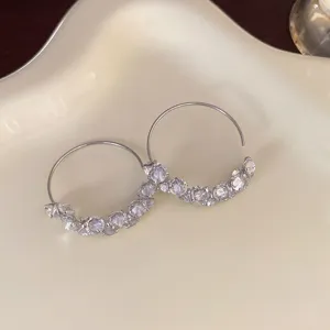 Primo piano dettagliato di orecchini a cerchio con strass su un vassoio di ceramica.