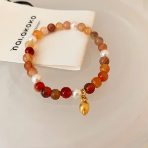 Detailed view of red agate and pearl beaded bracelet with charming gold pendant design.