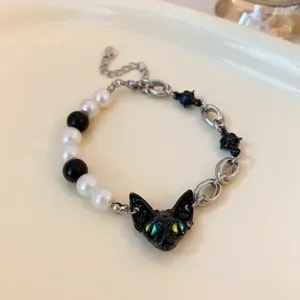 Detail shot of a unique black cat pearl bracelet, featuring green eyes, white beads and sleek metal chain links.