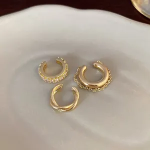Detailaufnahme von drei minimalistischen Goldohrringen mit Zirkon und Kettendesign.