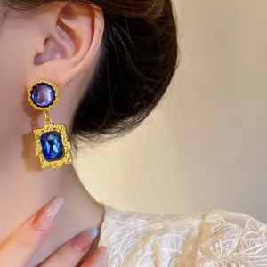 Detailaufnahme von goldenen geometrischen Vintage-Ohrringen mit blauen Kristallsteinen.