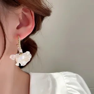 Close-up detail of sweet pearl and white flower petal earrings, elegant gold-plated finish.