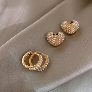 Close-up of retro gold-plated heart and hoop earrings decorated with delicate small white pearls.