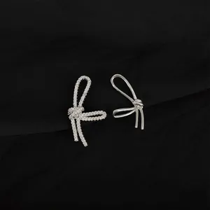 Closeup of asymmetrical bow earrings featuring sparkling zircon and smooth metal design.