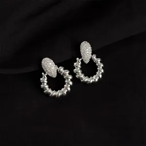 Silver metal twisted hoop earrings with pavé crystal top, trendy chic daily fashion detail shot.