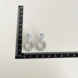 Detailed view of silver clip-on earrings with twisted hoop design and sparkling rhinestones.