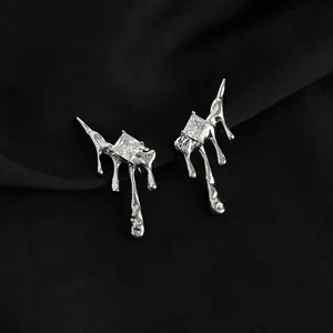 Close-up detail of silver metallic melting drip earrings with square cubic zirconia stones.