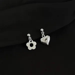 Close-up detail of trendy asymmetric silver clip-on earrings featuring cute flower and heart charms.