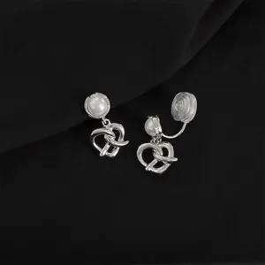 Close-up shot of silver clip-on earrings featuring a pearl top and twisted knot pendant.