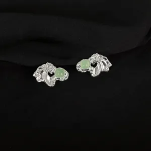 Close-up of unique metal clip earrings featuring green stone accents, intricate design.
