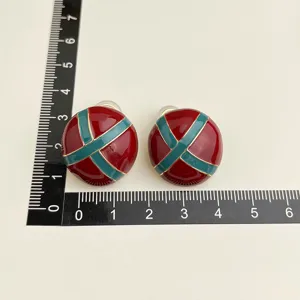 Detail view of vintage burgundy and green enamel clip-on earrings with gold trim sizing.
