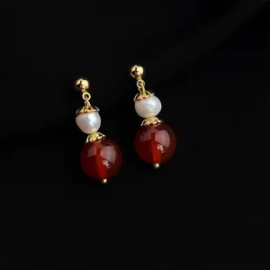 Detailed closeup of elegant vintage gold plated pearl and red bead drop earrings.