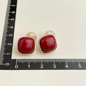 Detailed shot of vintage burgundy square clip-on earrings with gold rim and measurement scale.