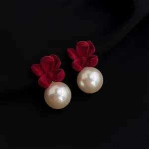 Close-up detail of vintage red velvet bow and pearl earrings with elegant texture.