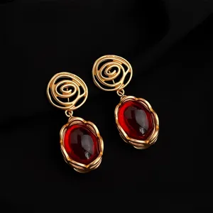 Detailed close-up of vintage gold-plated drop earrings featuring bold spiral tops and red stones.