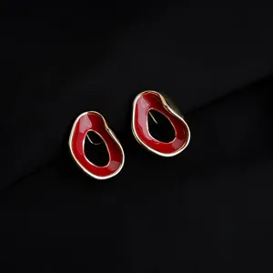 Close-up detail view of irregular gold-rimmed red enamel clip-on earrings, elegant retro style.