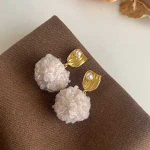 Detailaufnahme trendiger Herbst Winter flauschige Pompom Ohrringe mit Gold und Perle.