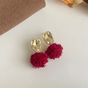 Nahaufnahme von süßen Plüschball-Ohrringen mit goldenen unregelmäßigen Metallsteckern.