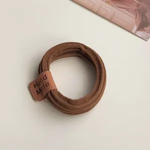 Close-up detail of a brown elastic hair tie featuring a charming handmade leather label.
