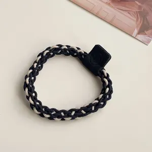 Detailed close-up shot of a black and beige braided hair tie with a chic leather patch accent.