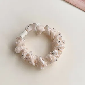 Close-up detail of elegant champagne satin hair scrunchie with sparkling rhinestones and connector.