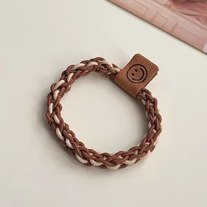 Brown braided hair tie with leather smiley tag, elegant milk tea color hair accessory.