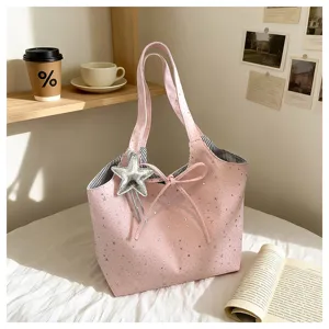 Pink tote bag with silver star pattern and star pendant, lifestyle detail view on white bed.