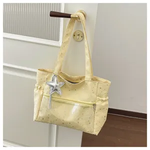 Dettaglio borsa a spalla gialla con stampa stelle, tasca frontale trasparente e ciondolo.