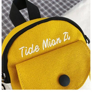 Close up view of yellow canvas mini backpack front pocket detail with letter print.