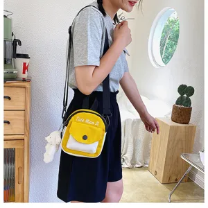 Canvas crossbody bag detail view, yellow and white small shoulder bag with cute bear pendant.