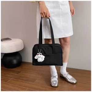 Detail shot of a black tote shoulder bag with a cute white puppy keychain held by a model.