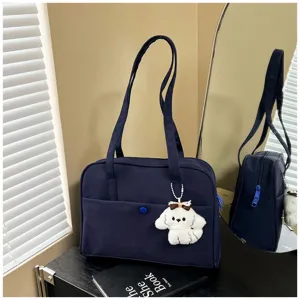 Detailed view of dark blue tote shoulder bag with cute puppy plush charm on dark desk.