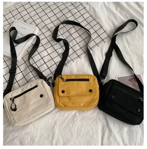 Dettaglio della borsa a tracolla in tela con opzioni di colore, cinghie e tasche anteriori.