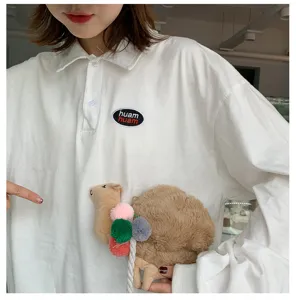 Dettaglio borsa a tracolla cammello in peluche, simpatico design animale con pompon colorati.