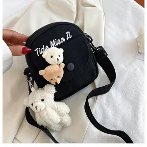 Black canvas crossbody bag with cute plush bear charms and trendy letter embroidery detail.