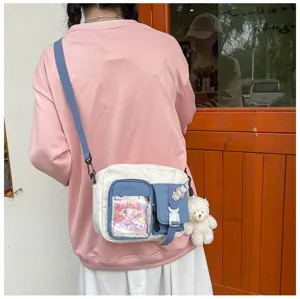 Détail de sac bandoulière en toile avec poche transparente, multi compartiments et pendentif.