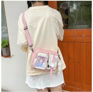 Vue détaillée du sac bandoulière en toile rose avec une poche fenêtre et un pendentif.