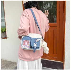 Détail de sac bandoulière en toile avec poche transparente, motif anime et pendentif.