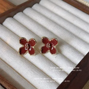 Orecchini a lobo fiore smalto rosso vintage, dettaglio gioiello bordo oro elegante.
