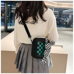 Detail shot of black canvas crossbody bag with green checkered pattern and cute plush toy pendant.