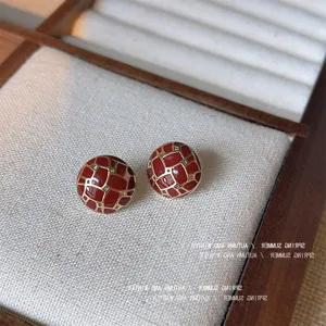 Primo piano di orecchini a lobo geometrici smaltati in rosso vintage e oro dettaglio.