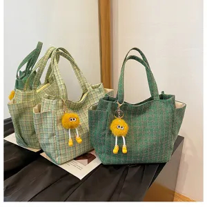 Detailed view of green plaid shoulder tote bag with cute plush yellow monster pendant.