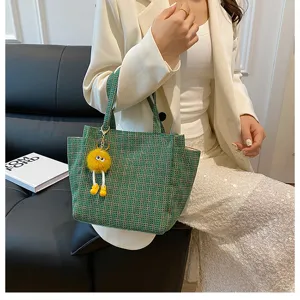 Close-up view of a green woven knit tote bag featuring a cute yellow plush charm detail.