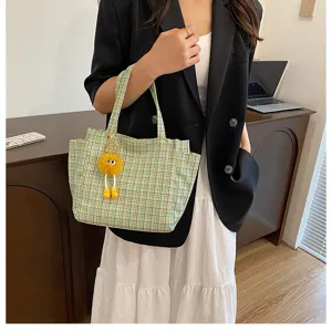Detailed shot showing the stylish green plaid tote bag with cute yellow plush charm in use.