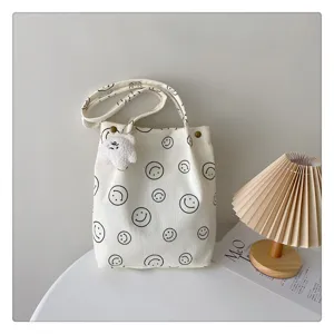 White corduroy tote bag detail showing black smiley face print and cute plush pendant close up.