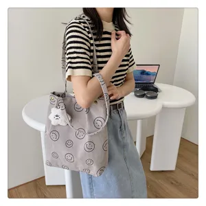 Corduroy shoulder bag featuring cute smiley face print and plush pendant detail for daily use.